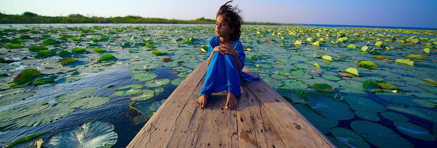 Girl sitting on a boat among lotus leaves on the lake